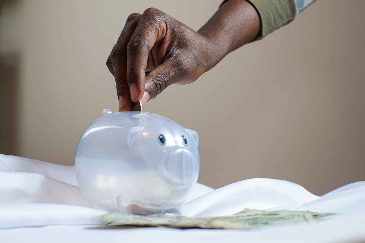 Crafting Captivating Headlines: Your awesome post title goes here Close-up of a person's hand placing coins into a transparent piggy bank to save money.